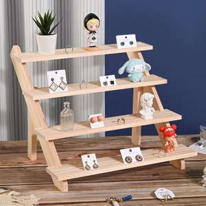 May include: A wooden tiered shelf display with four shelves. The shelves are angled and the display is made of natural wood. The shelves are decorated with small figurines, jewelry, and other decorative items.