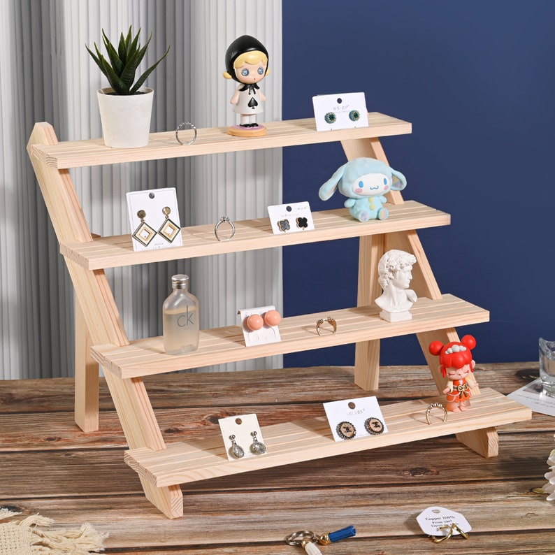 May include: A wooden tiered shelf display with four shelves. The shelves are angled and the display is made of natural wood. The shelves are decorated with small figurines, jewelry, and other decorative items.