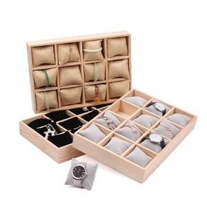 May include: A wooden jewellery display box with multiple compartments. The box has two layers, the top layer has 12 compartments with beige fabric cushions and the bottom layer has 12 compartments with black velvet cushions. The box is ideal for storing and displaying jewellery, watches, and other small items.
