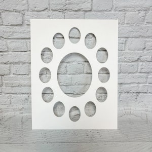 May include: White cardstock with a large oval cutout in the center and 12 smaller oval cutouts around the edge. The cardstock is on a white brick background.
