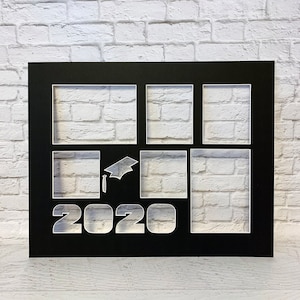 May include: Black photo frame with six openings, a graduation cap, and the year "2020" cut out. The frame is set against a white brick wall background. Ideal for displaying graduation photos.