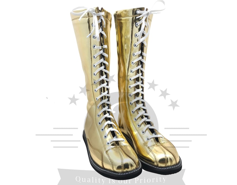 K&ouml;nnte beinhalten: Ein Paar goldfarbene, kniehohe Stiefel mit wei&szlig;en Schn&uuml;rsenkeln. Die Stiefel haben eine gl&auml;nzende, metallische Oberfl&auml;che und eine schwarze Sohle. Die Schn&uuml;rsenkel sind oben gebunden. Kost&uuml;m- oder Performance-Stiefel.