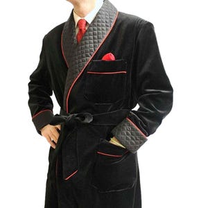 May include: A black velvet robe with a red trim and a quilted black lining. The robe has a shawl collar, a tie belt, and two pockets.