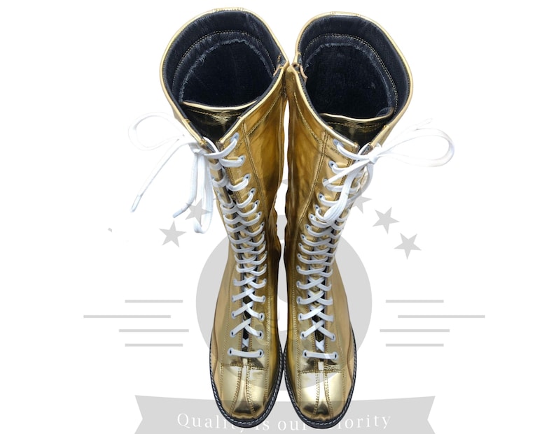 K&ouml;nnte beinhalten: Ein Paar goldfarbene, kniehohe Stiefel mit wei&szlig;en Schn&uuml;rsenkeln. Die Stiefel haben eine gl&auml;nzende, metallische Oberfl&auml;che und eine schwarze Sohle. Die Schn&uuml;rsenkel verlaufen &uuml;ber die Vorderseite der Stiefel, und die Oberseite der Stiefel hat ein schwarzes Innenfutter.