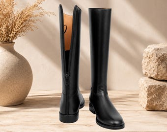 May include: A pair of black knee-high boots with a smooth finish. One boot is shown from the back, featuring a full-length vertical zipper that is partially open, revealing a tan interior lining. The other boot is shown from the side profile.