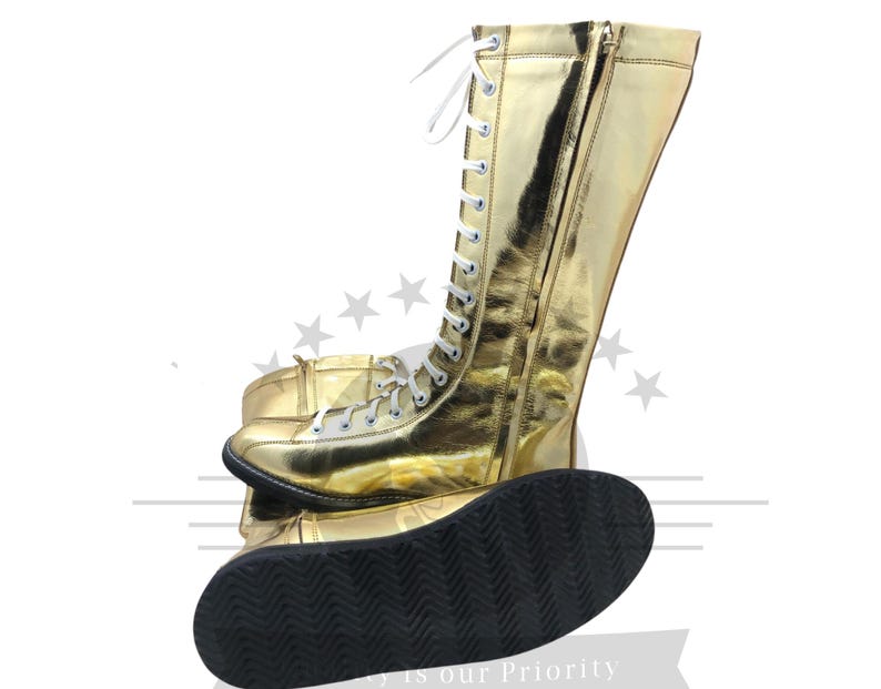 K&ouml;nnte beinhalten: Ein Paar goldfarbene, hoch geschnittene Stiefel mit wei&szlig;en Schn&uuml;rsenkeln und einem Rei&szlig;verschluss. Die Stiefel haben eine gl&auml;nzende, metallische Oberfl&auml;che und eine schwarze, strukturierte Sohle. Sportschuhe.