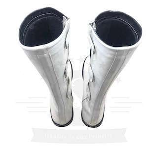 May include: A pair of white leather boots with black accents and buckles. The boots are knee-high and have a pointed toe.