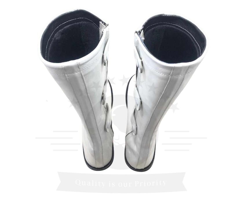 May include: A pair of white leather boots with black accents and buckles. The boots are knee-high and have a pointed toe.
