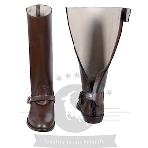 May include: A pair of brown leather riding boots with a zipper on the back and a buckle strap at the top. The boots are shown with the inside of the boot facing out.
