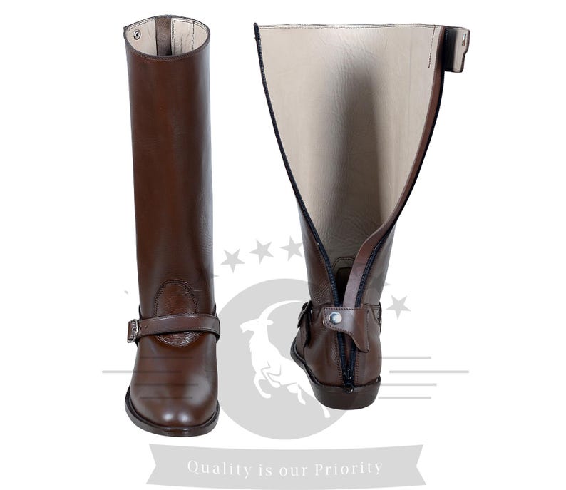 May include: A pair of brown leather riding boots with a zipper on the back and a buckle strap at the top. The boots are shown with the inside of the boot facing out.