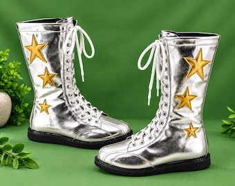 May include: A pair of mid-calf boots in a metallic silver finish featuring white lace-up closures and black soles. Each boot is decorated with three gold-colored star appliques of varying sizes positioned along the outer side of the shaft.