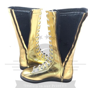 K&ouml;nnte beinhalten: Ein Paar goldfarbene kniehohe Stiefel mit wei&szlig;en Schn&uuml;rsenkeln und einem Rei&szlig;verschluss. Die Stiefel haben eine gl&auml;nzende, metallische Oberfl&auml;che und eine schwarze Sohle. Die Innenseite ist schwarz. Der Text "Quality is our Priority" steht unten.