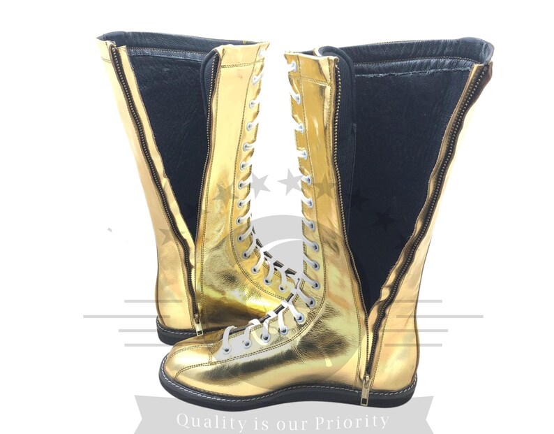 K&ouml;nnte beinhalten: Ein Paar goldfarbene kniehohe Stiefel mit wei&szlig;en Schn&uuml;rsenkeln und einem Rei&szlig;verschluss. Die Stiefel haben eine gl&auml;nzende, metallische Oberfl&auml;che und eine schwarze Sohle. Die Innenseite ist schwarz. Der Text "Quality is our Priority" steht unten.