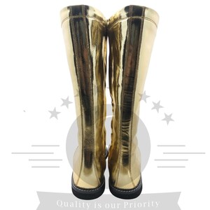 K&ouml;nnte beinhalten: Ein Paar kniehohe goldene Stiefel mit gl&auml;nzendem, metallischem Finish. Die Stiefel haben eine schwarze Sohle und ein schlichtes Design, geeignet f&uuml;r Kost&uuml;me oder Mode. Die Aufnahme zeigt die Stiefel von hinten, die volle H&ouml;he.