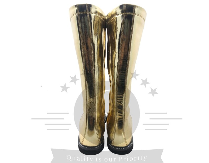 K&ouml;nnte beinhalten: Ein Paar kniehohe goldene Stiefel mit gl&auml;nzendem, metallischem Finish. Die Stiefel haben eine schwarze Sohle und ein schlichtes Design, geeignet f&uuml;r Kost&uuml;me oder Mode. Die Aufnahme zeigt die Stiefel von hinten, die volle H&ouml;he.