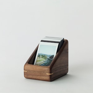 May include: A wooden photo holder with a triangular shape and a light brown finish. The holder is filled with instant photos.