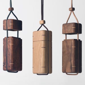 Può includere: Tre lampade a sospensione in legno con forme rettangolari e quadrate. Le lampade sono sospese da corde e presentano un mix di tonalità di legno scuro e chiaro. Il design include accenti metallici e un'estetica minimalista.