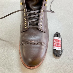 May include: Brown leather lace-up boots with gold eyelets and a decorative stitch pattern around the toe. The boots are tied with brown laces and come with a spare set of brown laces.