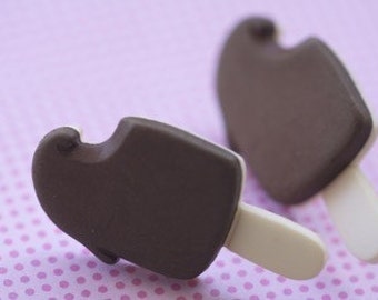 May include: Two brown chocolate ice cream popsicles with white sticks on a pink polka dot background.