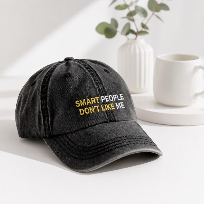 Puede incluir: Una gorra de b&eacute;isbol gris carb&oacute;n con acabado desgastado que presenta el texto bordado "SMART PEOPLE" en amarillo y "DON'T LIKE ME" en blanco en el panel frontal. La gorra tiene una visera curva y una corona estructurada con un bot&oacute;n.