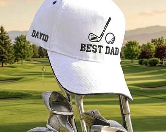 May include: White golf cap with black trim, featuring the text "DAVID" on the left and "BEST DAD" with a golf club and ball graphic. The cap is resting on golf clubs, with a golf course in the background.