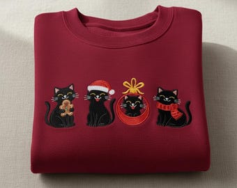 May include: A maroon sweatshirt with embroidered black cats in Christmas outfits. One cat holds a gingerbread man, another wears a Santa hat, a third is in an ornament, and the last has a red scarf.