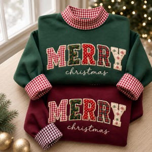 May include: A dark green sweatshirt and a maroon sweatshirt, each featuring a high collar with red and white gingham trim. The word MERRY is appliqued in patterned fabric letters, with the word christmas embroidered below in white cursive script.