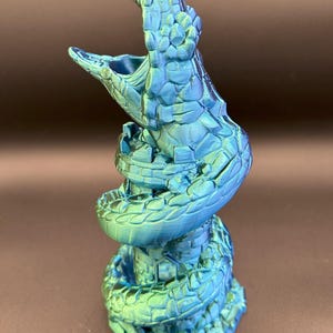 May include: A 3D printed green and blue snake figurine with a textured surface. The snake is coiled around a tower.