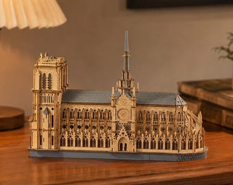 May include: A detailed wooden model of the Notre-Dame Cathedral featuring intricate architectural elements, including a tall central spire, a rose window, and a square tower, all constructed from light-colored wood with blue-gray roof accents.