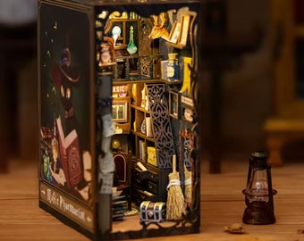 May include: A miniature wooden dollhouse shaped like a book, with a dark green and brown exterior. The book is open to reveal a detailed interior with a bookshelf, a table, a chair, and a chest. The book's cover reads "Magic Pharmacia".