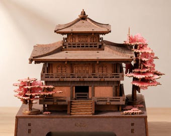 May include: A wooden model of a multi-story temple structure featuring dark brown panels, intricate architectural details, and two attached trees with pink blossoms. The base of the model includes the text Rolife engraved on the front panel.