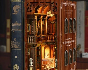 Puede incluir: Un rincón de libro de madera con un interior detallado que representa una escena de biblioteca. El exterior del rincón del libro es marrón con el texto "The Philosophical Library". Un libro azul está a la izquierda.