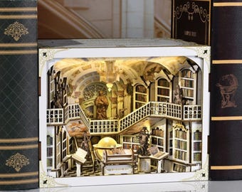 May include: A miniature library diorama with intricate details, including bookshelves, statues, and a grand staircase. The diorama is illuminated, showcasing the interior. Flanking the diorama are two large, dark green and brown books.