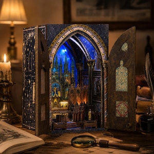 Könnte beinhalten: Ein hölzernes Book-Nook-Diorama mit einem offenen gotischen Kathedralen-Innenraum, blauer LED-Beleuchtung, filigranen architektonischen Details und Miniaturfiguren. Die Außenseite ist dunkelblau mit goldenen Sternenmustern.