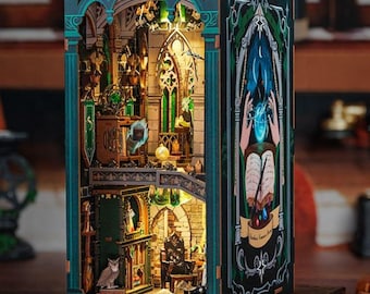 Könnte beinhalten: Ein Miniaturmodell aus Holz einer magischen Bibliothek in Grün- und Goldtönen. Das Modell verfügt über einen detaillierten Innenraum mit Bücherregalen, einem Schreibtisch und einer magischen Eule. Die Vorderseite des Modells zeigt eine gemalte Szene eines Zauberers, der einen Zauber wirkt.