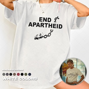Puede incluir: Una camiseta blanca de manga corta con el texto negro END APARTHEID junto a un gráfico de una cadena rota y una figura de palo. La camiseta incluye un pequeño recuadro circular que muestra la prenda puesta y un menú de selección de colores.