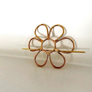 Puede incluir: Una pinza para el pelo de metal dorado en forma de flor con una barra de metal larga y delgada que se extiende desde el centro.