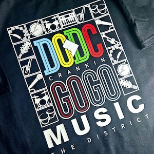 May include: Black t-shirt with a white graphic design featuring the text "DC Crank'n Go-Go Music The District" with colourful musical instruments in a grid pattern.