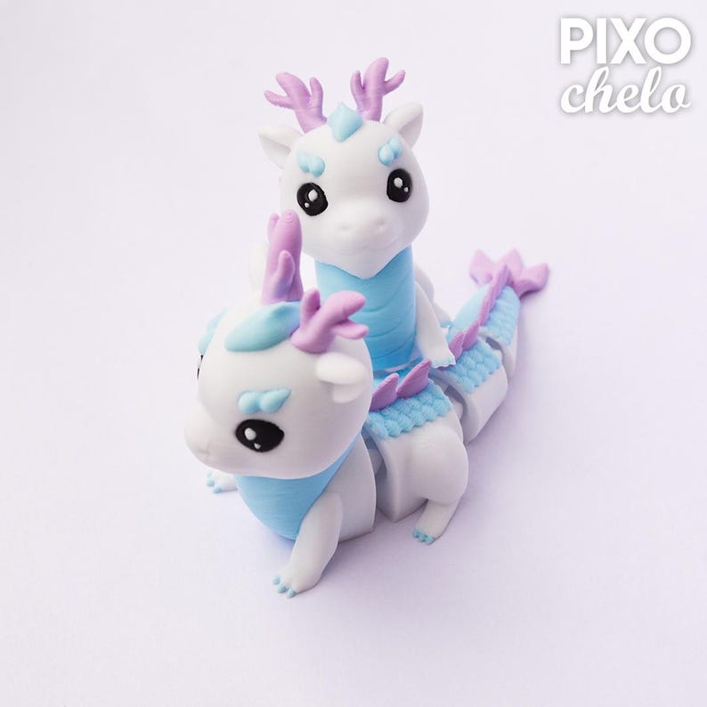 Peut inclure: Deux figurines de dragons blancs avec des d&eacute;tails bleus et violets. Les dragons ont de grands yeux noirs, des cols bleus et des bois violets. L'un est perch&eacute; sur le dos de l'autre, qui a un corps segment&eacute;.