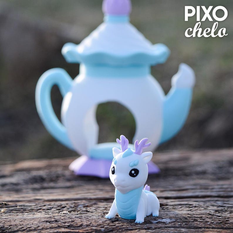 Peut inclure: Une th&eacute;i&egrave;re en c&eacute;ramique blanche et bleue avec une figurine assortie d'un dragon blanc avec des bois violets et une &eacute;charpe bleue. La th&eacute;i&egrave;re a un bord festonn&eacute; et un dessus violet. La figurine est devant la th&eacute;i&egrave;re.