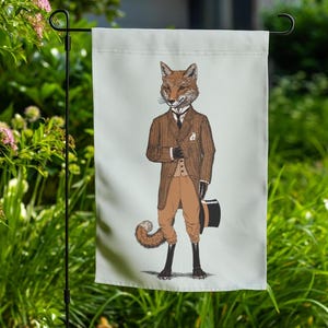 Op de afbeelding: Een witte tuin vlag met een cartoon illustratie van een vos die een bruin pak, een wit overhemd en een zwarte hoed draagt. De vos staat met zijn rechterhand in zijn zak en zijn linkerhand houdt de hoed vast.