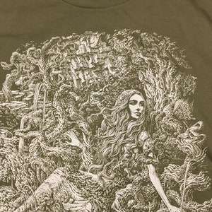 A detailed image of a long haired beautiful woman enveloped in branches, rocks, ferns and flowers printed on a mens shirt.