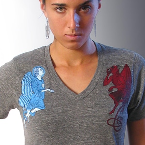 May include: A heather grey t-shirt with a blue angel and a red devil graphic print. The angel is on the left side of the shirt and the devil is on the right side.