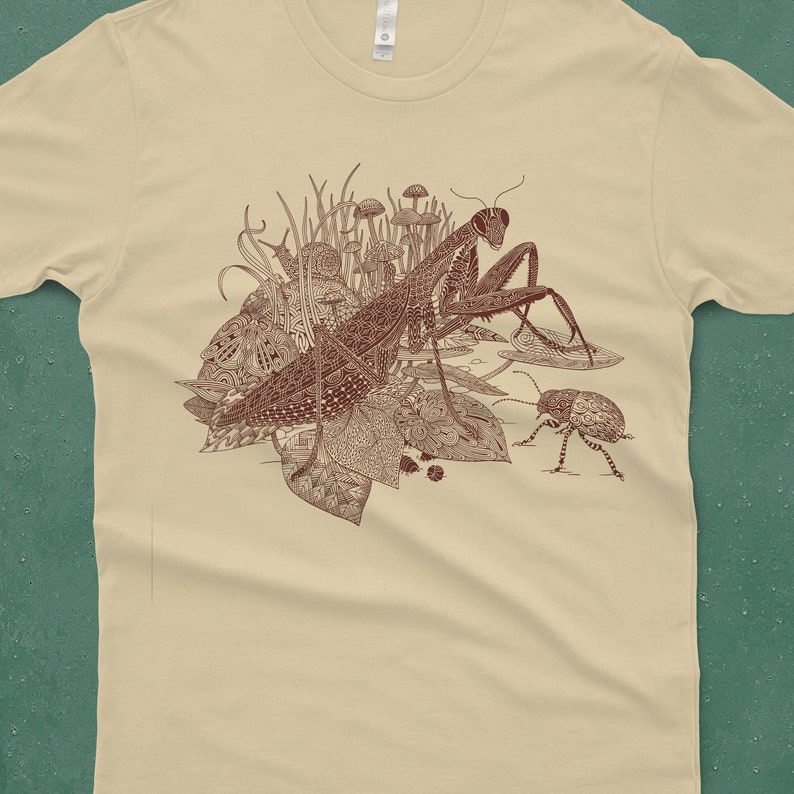 An intricate drawing of a praying mantis, snail, beetle and mushrooms, screen printed on a cream colored unisex-mens T-shirt in front of a blue green backdrop