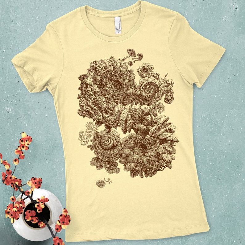 Op de afbeelding: Lichtgele t-shirt met een sepia-getinte illustratie van een abstract, organisch ontwerp. Het kunstwerk bevat wervelende vormen, paddenstoelachtige vormen en ingewikkelde texturen. Het shirt heeft een klassieke ronde hals en korte mouwen.