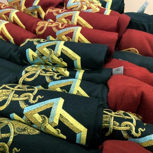 Screen printed graphic T-shirts in red and black with a yellow, gold and blue geometric structure on it. There are tentacles weaving through the strange structure on this men's clothing.