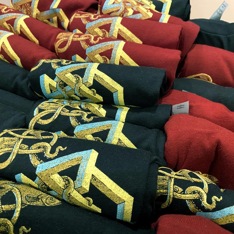 Screen printed graphic T-shirts in red and black with a yellow, gold and blue geometric structure on it. There are tentacles weaving through the strange structure on this men's clothing.