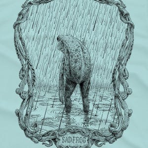 A drawing of a sad frog standing in the rain, surrounded by an ornate border. Screen printed onto a blue, Next Level brand T-shirt.