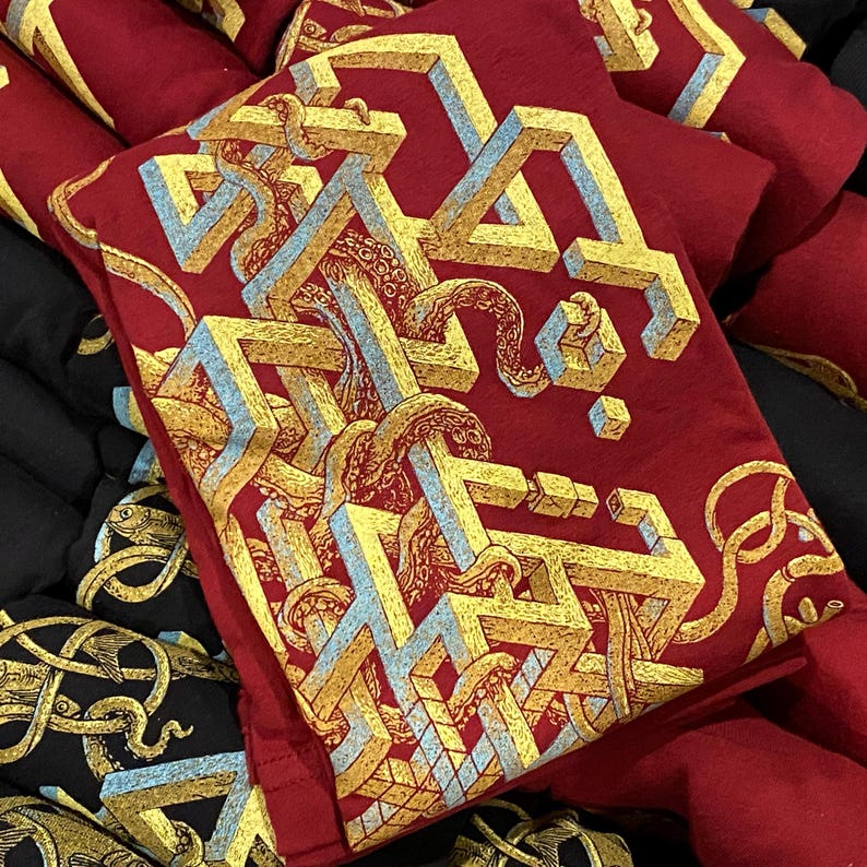 Screen printed graphic T-shirts in red and black with a yellow, gold and blue geometric pattern on it. There are tentacles weaving through the strange structure.