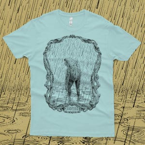A drawing of a sad frog standing in the rain, surrounded by an ornate border. Screen printed onto a blue, Next Level brand T-shirt.